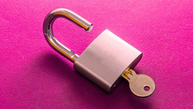 Open silver padlock with brass key rests on vibrant pink background