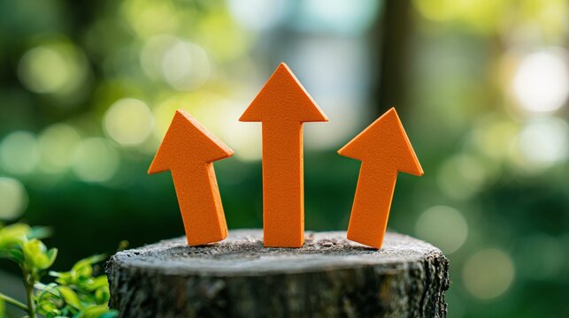 Three Vibrant Orange Upward Arrows Symbolizing Growth, Progress, and Success on a Natural Wood Stump in a Softly Blurred Green Outdoor Environment