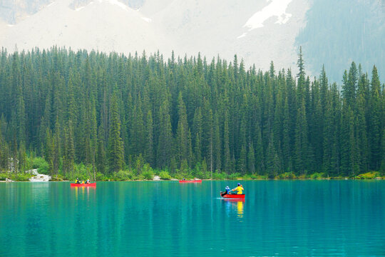 Several Groups of People in Red Canoes Floating on Brilliant Blue Lake in the Wilderness Mountains Enjoying Nature Outdoors