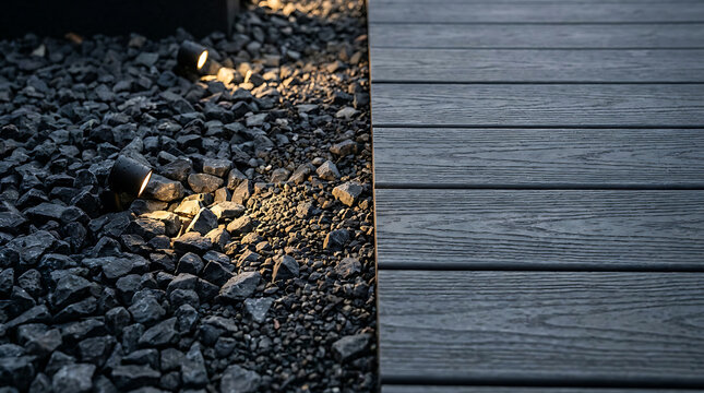 Close up of dark composite deck boards next to gravel with accent lighting.