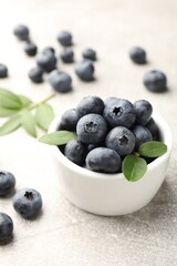 Fresh ripe blueberries in bowl and green leaves on grey table, closeup © New Africa