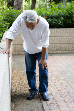 asian senior man with white hair holding painful knee from osteoarthritis, knee joint pain outdoor scene, full body shot