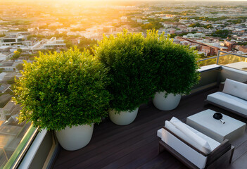 Obraz premium Rooftop terrace with potted green bushes and outdoor furniture overlooking a city at golden hour sunset, the modern urban landscape extends to the horizon under a warm, glowing sky