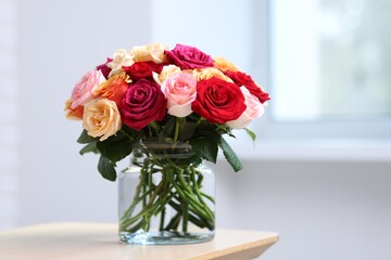 Obraz premium Beautiful bouquet of colorful roses in vase on wooden table indoors. Space for text