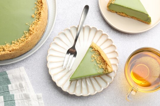 Tasty matcha cheesecake, server and cup of tea on light grey table, flat lay