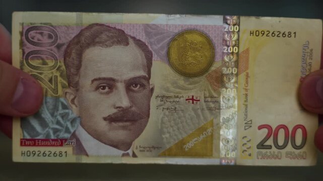 4K video close up. Male hand holds Georgian paper banknote 200 lari bill with portrait of prince Kaikhosro Cholokashvili, view of Sukhumi. Cash money, bank note of Georgia. Budget, financial crisis
