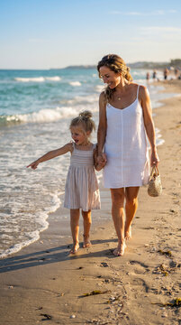 Madre e hija explorando la orilla de una playa y buscando conchas, representando naturaleza, infancia, familia, descubrimiento y vacaciones.