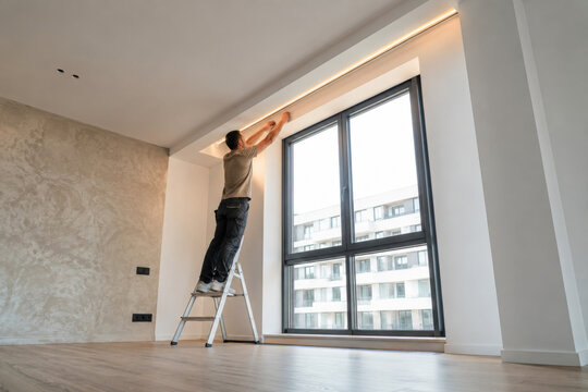Un hombre trabaja en la instalaci&oacute;n de luces en una ventana en un edificio moderno