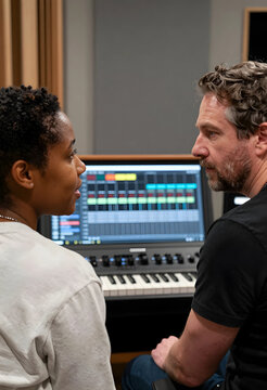 Music producers collaborating in a recording studio with a digital audio workstation and keyboard synthesizer