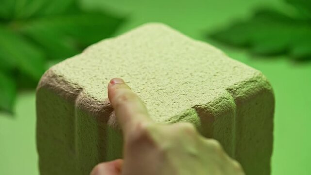 A person gently pressing their finger into a soft textured square foam block.