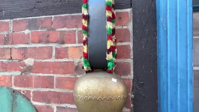 Camera Tilts Down Along Decorative Hanging Strap to Reveal Large Metal Bell on Brick Wall