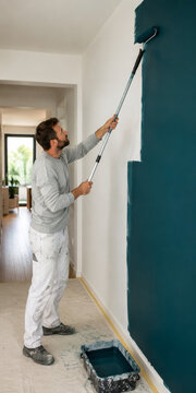 Un hombre pinta una pared de color azul en una casa moderna