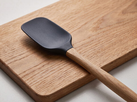 Black silicone spatula with a wooden handle lying on an oak cutting board