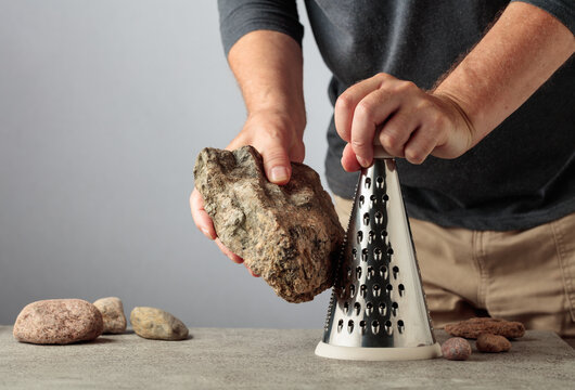 Man uselessly grating a stone on a kitchen grater, illustrating pointless work, wasted effort and inefficient processes.