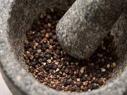 Black peppercorns being crushed with a pestle in a stone mortar