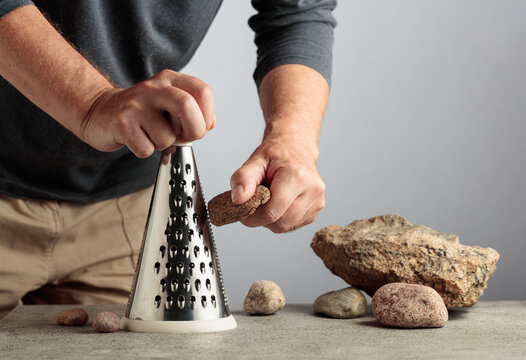 Man uselessly grating a stone on a kitchen grater, illustrating pointless work, wasted effort and inefficient processes.