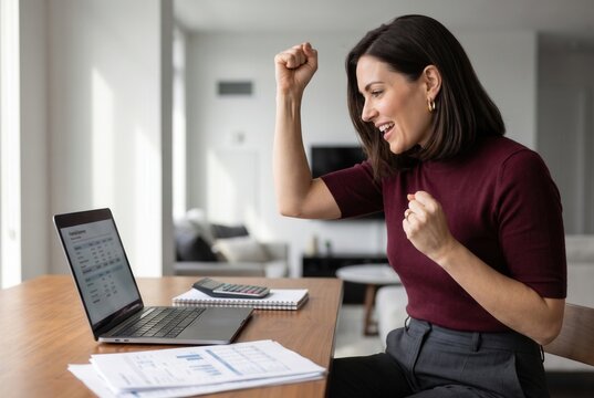 Businesswoman celebrating win, looking at laptop screen with fist pump