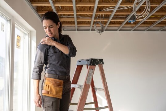 Woman feeling shoulder pain while working on a construction project inside a new building
