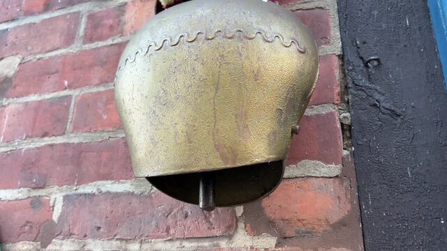 Close-Up of Large Weathered Metal Bell Hanging Against Old Red Brick Wall