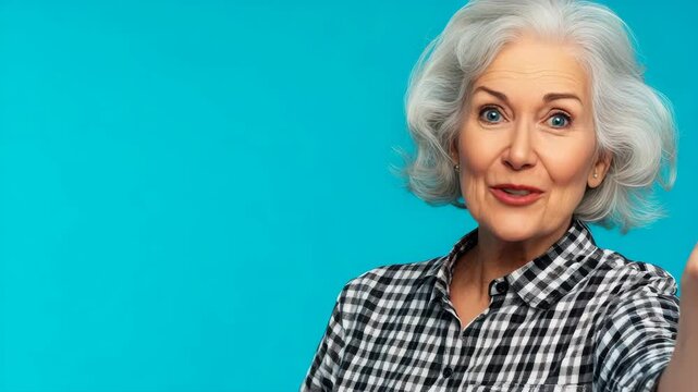 An attractive older woman with white curly hair and blue eyes, dressed in a patterned top, smiling warmly. She is looking directly at the camera with her hand on her hip.