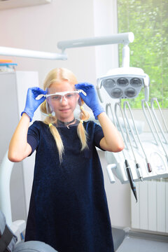 Little blonde girl in blue gloves puts transparent screen over her eyes and face. Dental office. Profession - dentist