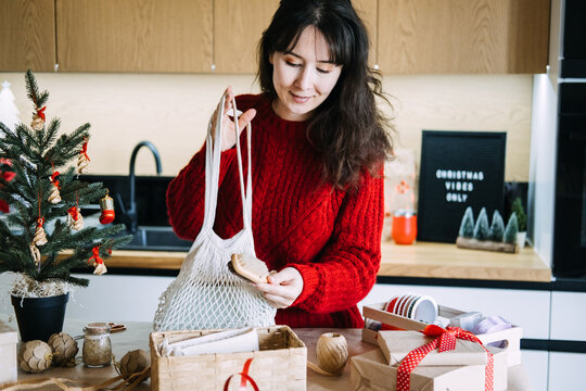Woman packs mesh bag and wooden brush into gift basket in kitchen near CHRISTMAS VIBES ONLY sign. Eco friendly gift basket, sustainable christmas gift set, zero waste gift ideas christmas