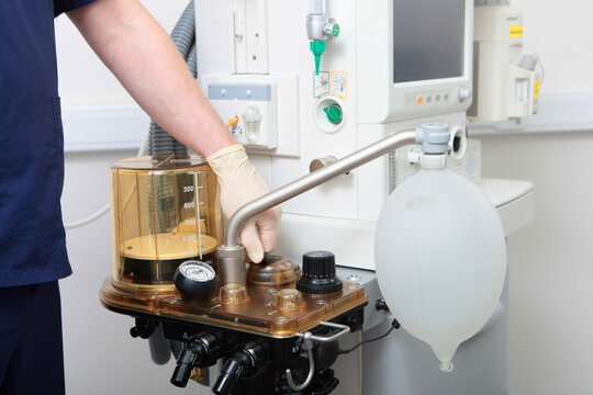 Anesthesiologist's hand in sterile glove adjusts metal port on control panel of anesthesia machine and breathing bag