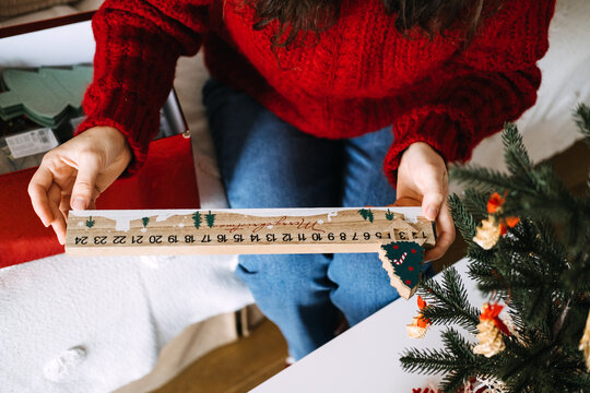 Woman hand holds wooden MERRY CHRISTMAS countdown calendar with sliding tree marker near decorated tree. Wooden christmas countdown, advent countdown calendar, handmade advent calendar