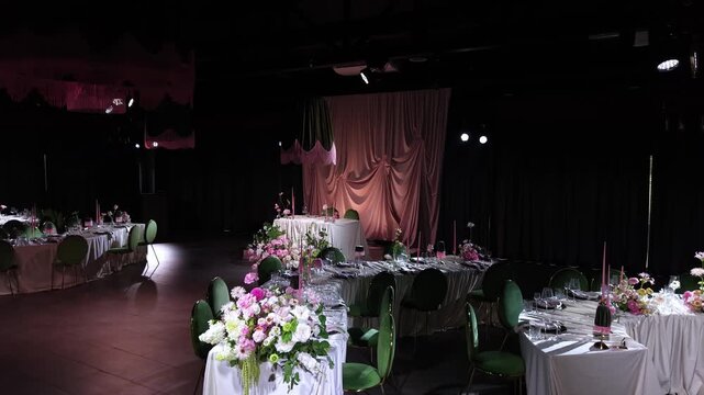 Beautifully decorated banquet hall ready for a wedding celebration or gala dinner, featuring tables adorned with fresh flowers, elegant tableware, and ambient lighting in a luxurious dark setting