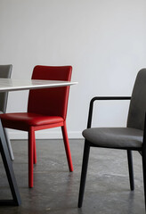 Fototapeta premium Modern red leather dining chair and gray fabric armchair with a white marble table in a minimalist interior, the room features a clean white wall and a concrete floor