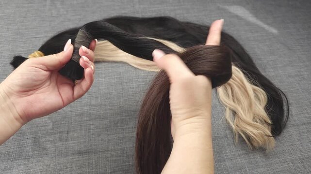 Close-up video of female hands displaying three sections of human hair extensions, showcasing different hair colors and textures for professional hair extension preparation, keratin bonding, wig makin