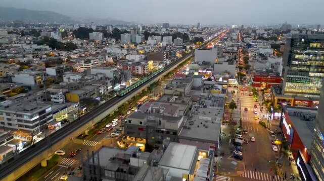 Cinematic aerial drone view of the Line 1 metro train crossing the San Borja district during a beautiful dusk in Lima, Peru.