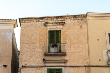 Historic building facade in Bari Italy with green shuttered balcony door and ornate cornice above weathered limestone wall in old town district © daily_creativity
