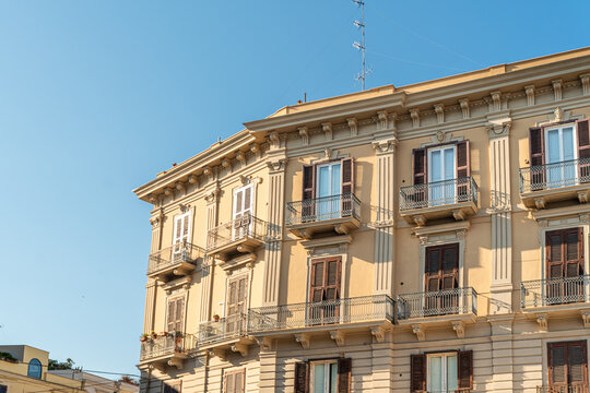 Classic Italian building facade in Bari, Italy featuring ornate neoclassical architecture with wrought iron balconies, brown shutters, and warm beige stone exterior
