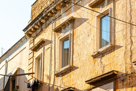 Historic building facade in Bari, Italy with weathered stone walls, ornate cornice, and modern windows bathed in warm golden afternoon light, concept of Mediterranean architecture