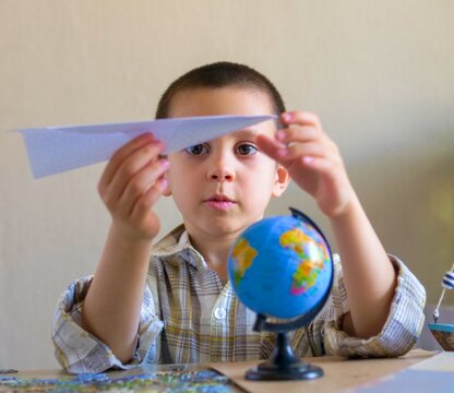 Focused young boy aiming a paper airplane over a world globe - Dreaming of flight: serious child holding a paper plane planning a global journey