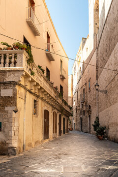 Bari Italy old town narrow alley with ornate stone balcony and terracotta facades leading through historic medieval quarter on sunny day