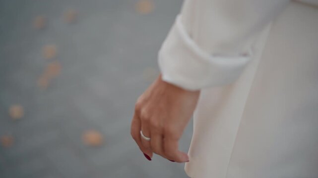 Cropped motion shot showing lower arm and relaxed hand beside pale long-sleeved coat or dress with rolled cuff, fabric hem and sleeve swaying gently as if walking or breeze moves garment; shallow