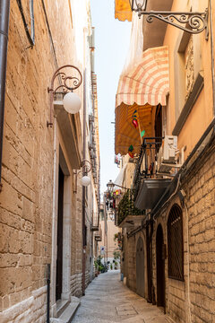 Bari Italy narrow alley in old town with stone buildings, striped awning, and wall-mounted globe lamps, concept of Mediterranean travel and historic architecture