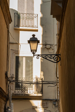 Narrow alley in Bari Italy with ornate wrought iron street lamp mounted on wall between old residential buildings with decorative balconies in warm afternoon light
