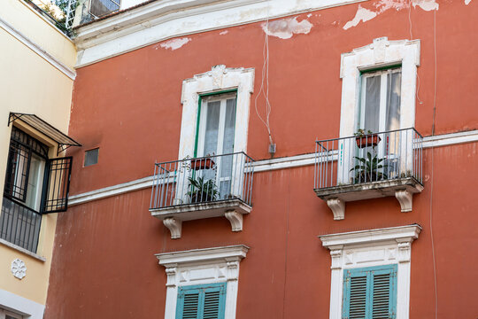 Bari Italy historic building facade with terracotta red walls, ornate white window frames, iron balconies with potted plants, and teal shutters in old town