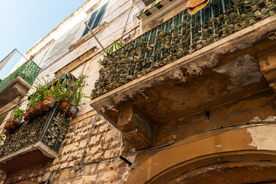 Bari Italy old town weathered stone balcony with pebbles and potted plants on deteriorating historic building facade, concept of urban decay and Mediterranean architecture