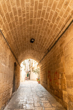 Bari Italy old town narrow stone alley with barrel vaulted ceiling leading to sunlit courtyard, ancient medieval architecture and cobblestone passage, concept of historic travel