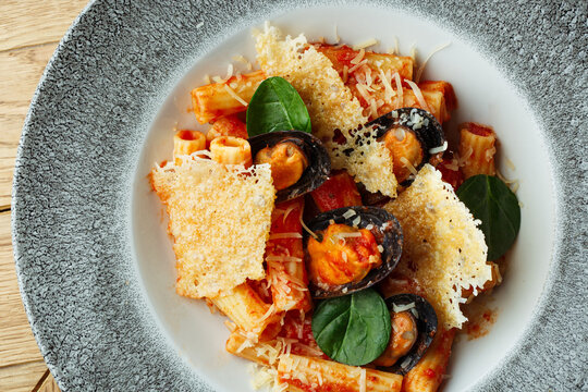 Seafood rigatoni with mussels, tomato sauce, fresh spinach and golden Parmesan cheese crisps