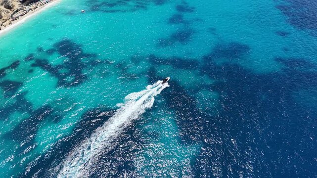 Aerial drone view of a speedboat cruising across the crystal-clear turquoise waters of the Ionian Sea near Saranda, Albania. Stunning Mediterranean coastline, white sandy beach, deep blue sea and spar