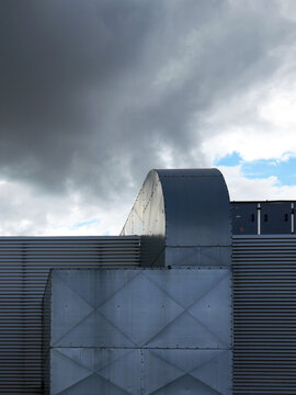 A large metal ventilation system extends from a corrugated metal building under a cloudy sky.