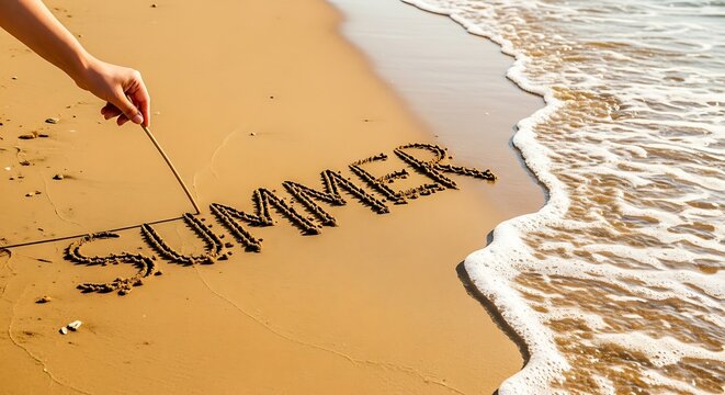 Hand writing SUMMER in the sand on a sunny beach with gentle waves lapping the shore.