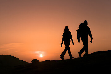 Obraz premium a couple in silhouette trekking through mountains as the sun sets