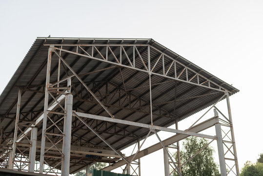A large metal framework is visible, showcasing the construction of an open building roof. The structure features angled supports and a clear sky in the background, indicating progress on the project