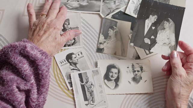 point of view of Wrinkled hands of a senior woman touching old black and white photographs of her youth